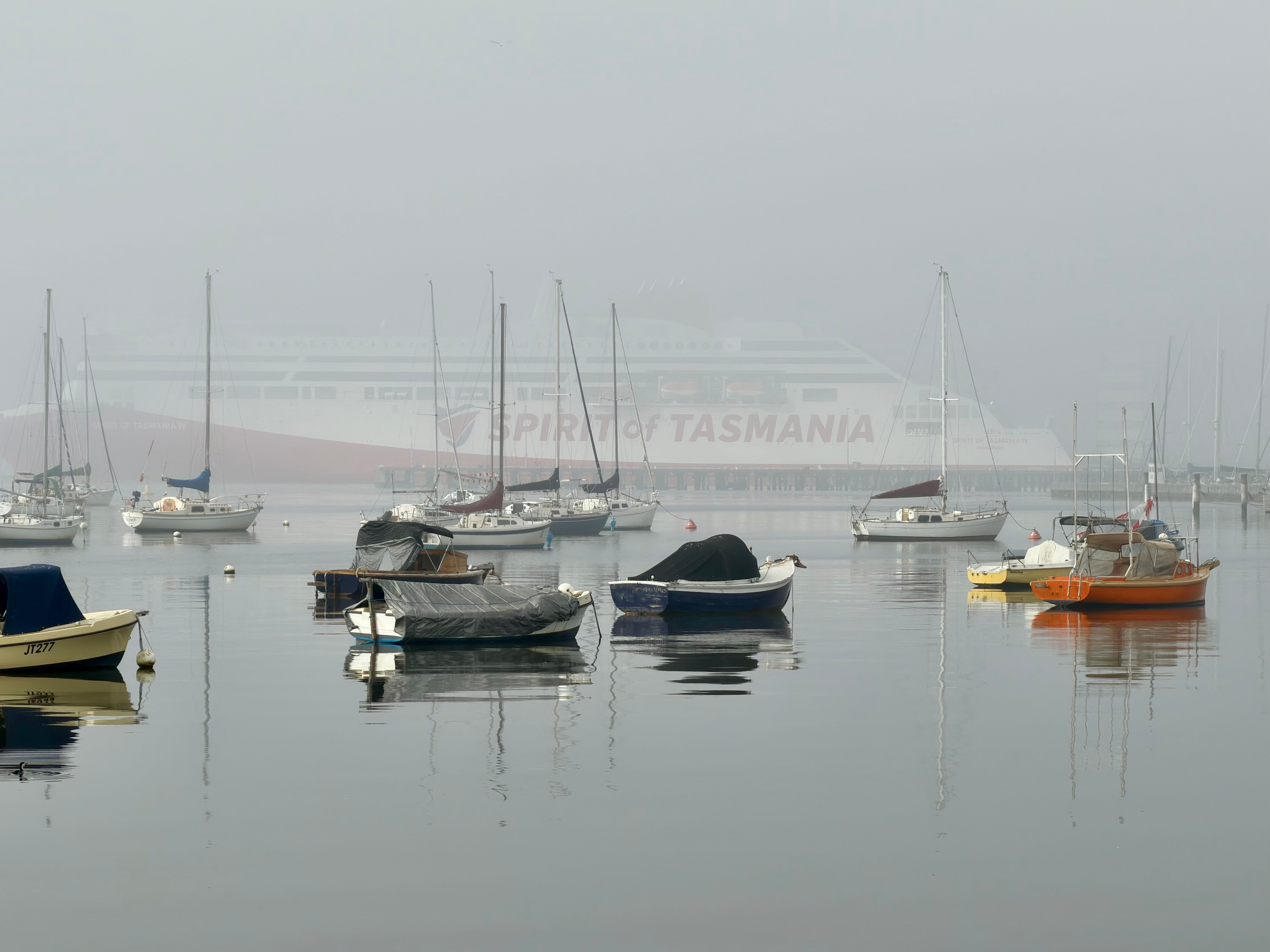 Peaceful scene of boats in foggy Williamstown harbor with Spirit of Tasmania ferry.
