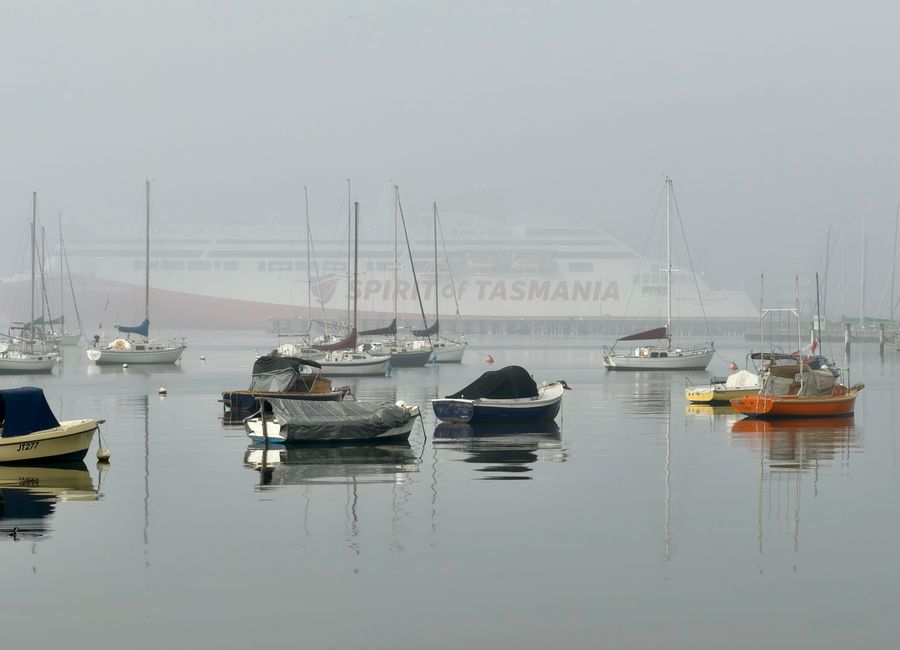 Peaceful scene of boats in foggy Williamstown harbor with Spirit of Tasmania ferry.