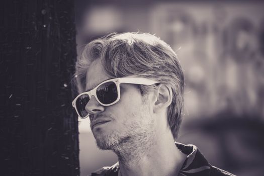 Black and white portrait of a man in sunglasses leaning against a city wall, exuding a cool and relaxed vibe.