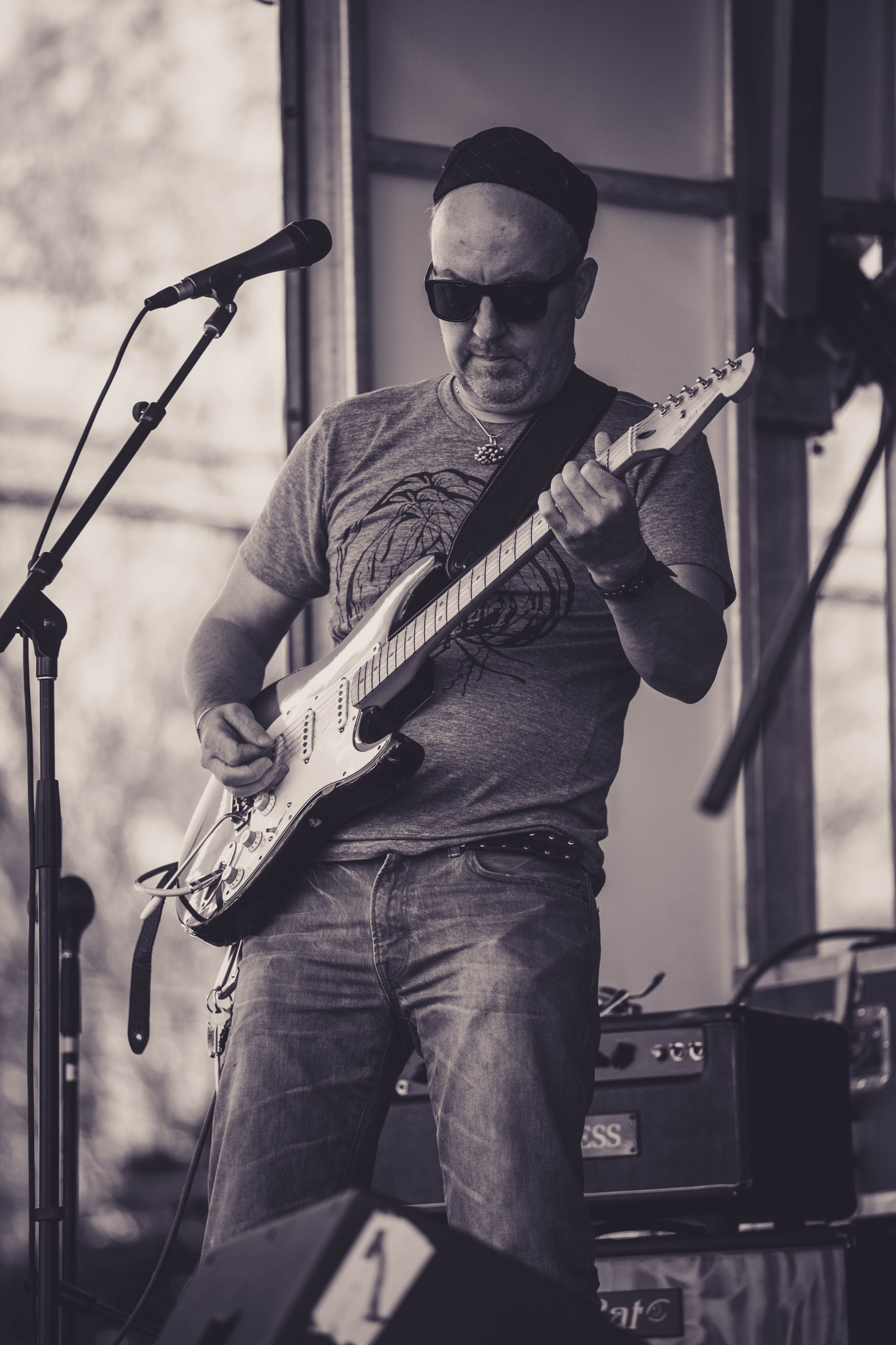 Black and white photo of a guitarist performing on stage at an outdoor concert.