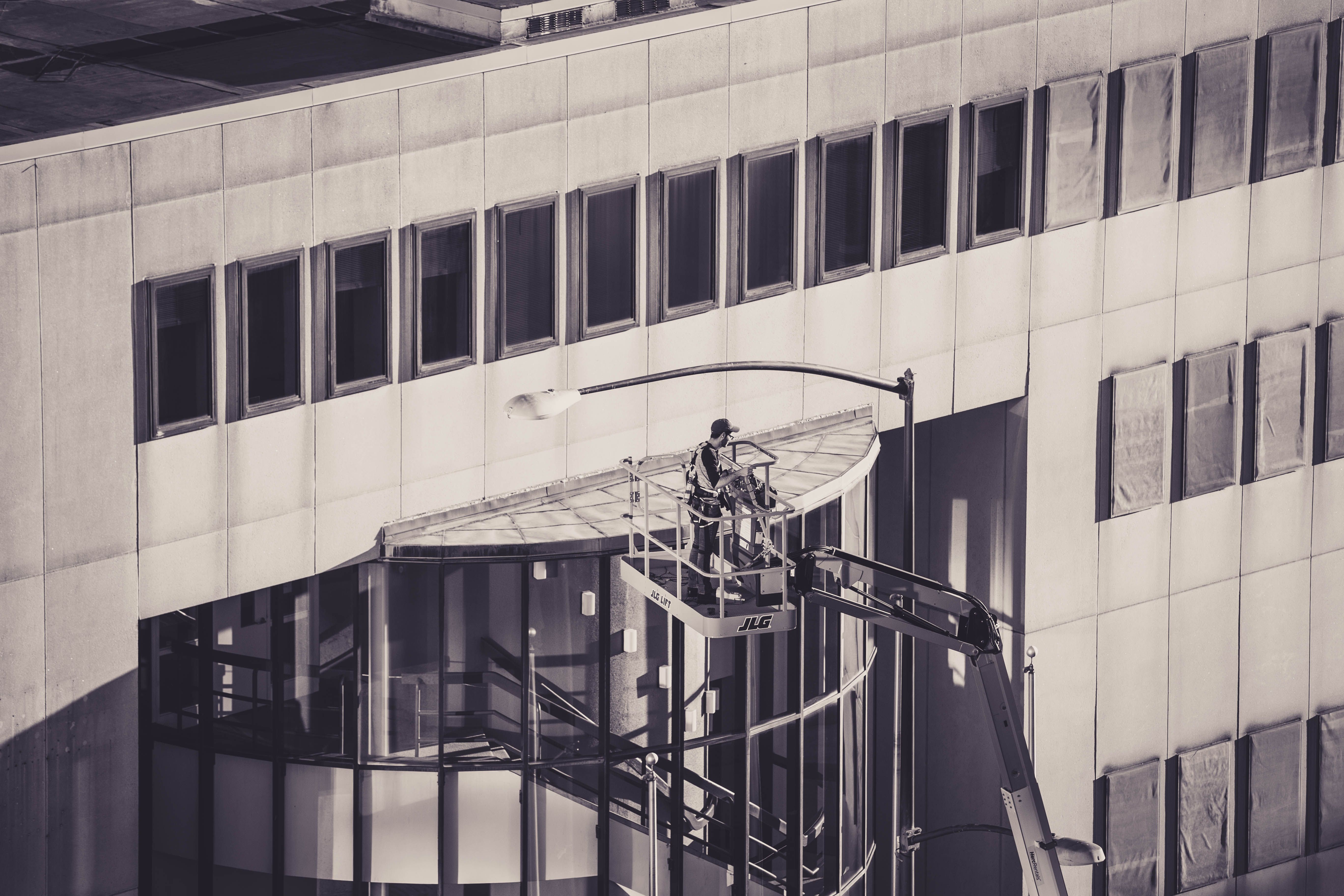 A construction worker on a hydraulic lift conducts maintenance on a modern building facade.