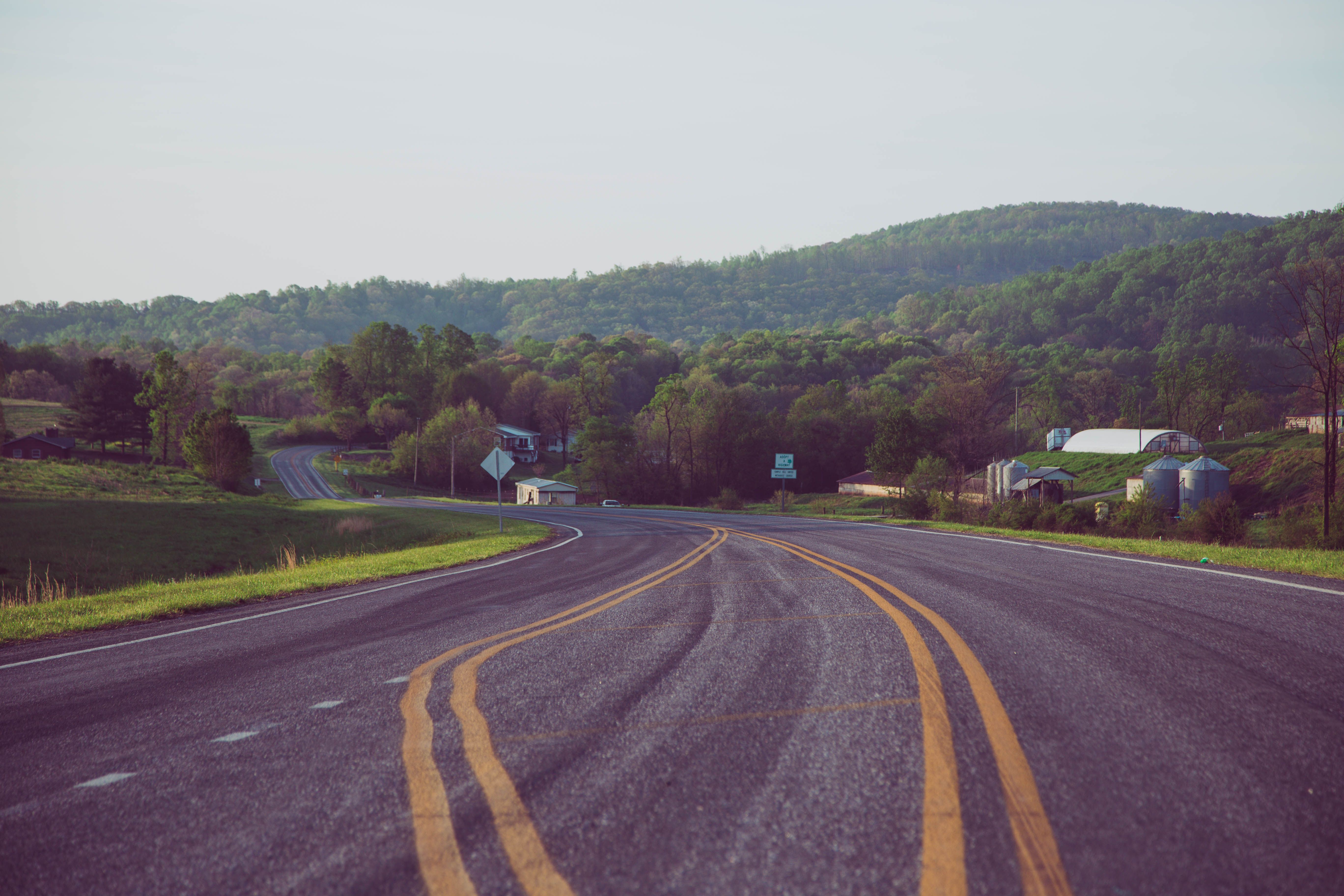 Peaceful country road winding through lush green hills under a clear sky.