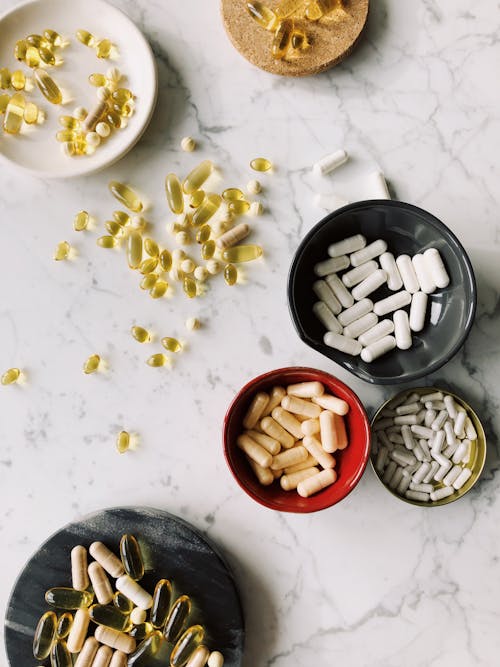 From above of different pills tablets drugs vitamins in various stands and plates assorted on marble tabletop in light room