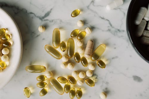 Top view of different capsules and pills placed on on desk between plates with medical remedy made to prevent vitamin deficiency