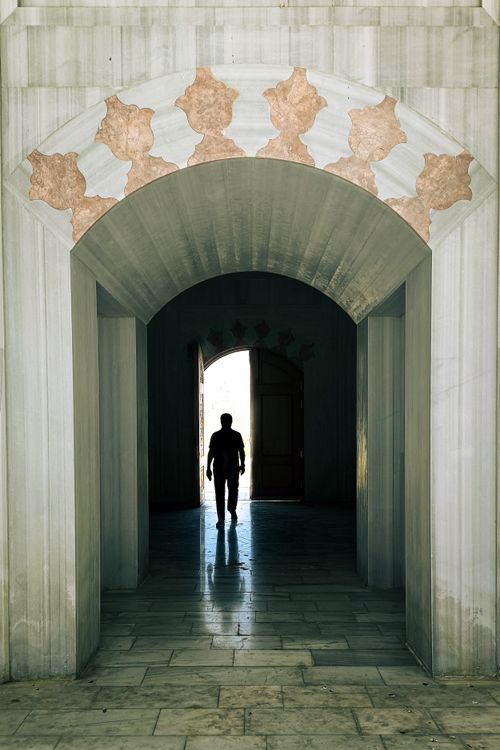 Free A lone silhouette walking through a historic archway passage. Stock Photo