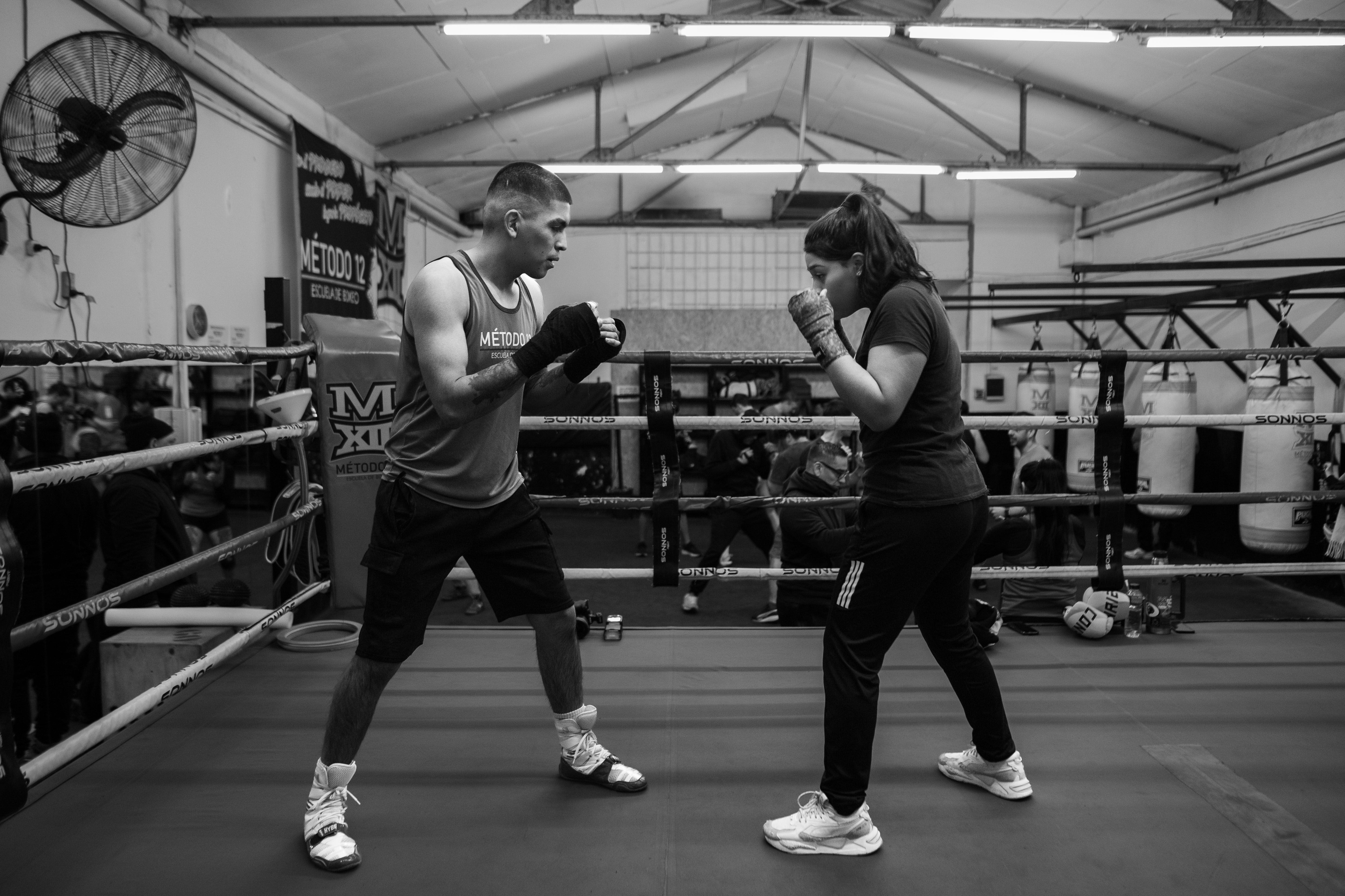 Two athletes sparring in a boxing ring indoors, showcasing rigorous training.