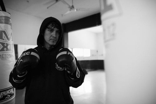 Free A focused boxer trains with a punching bag in a gym, wearing gloves and a hoodie. Stock Photo