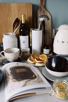 Top view of various types of tableware open cookbook and delicious homemade curd pancakes placed on table in cozy kitchen