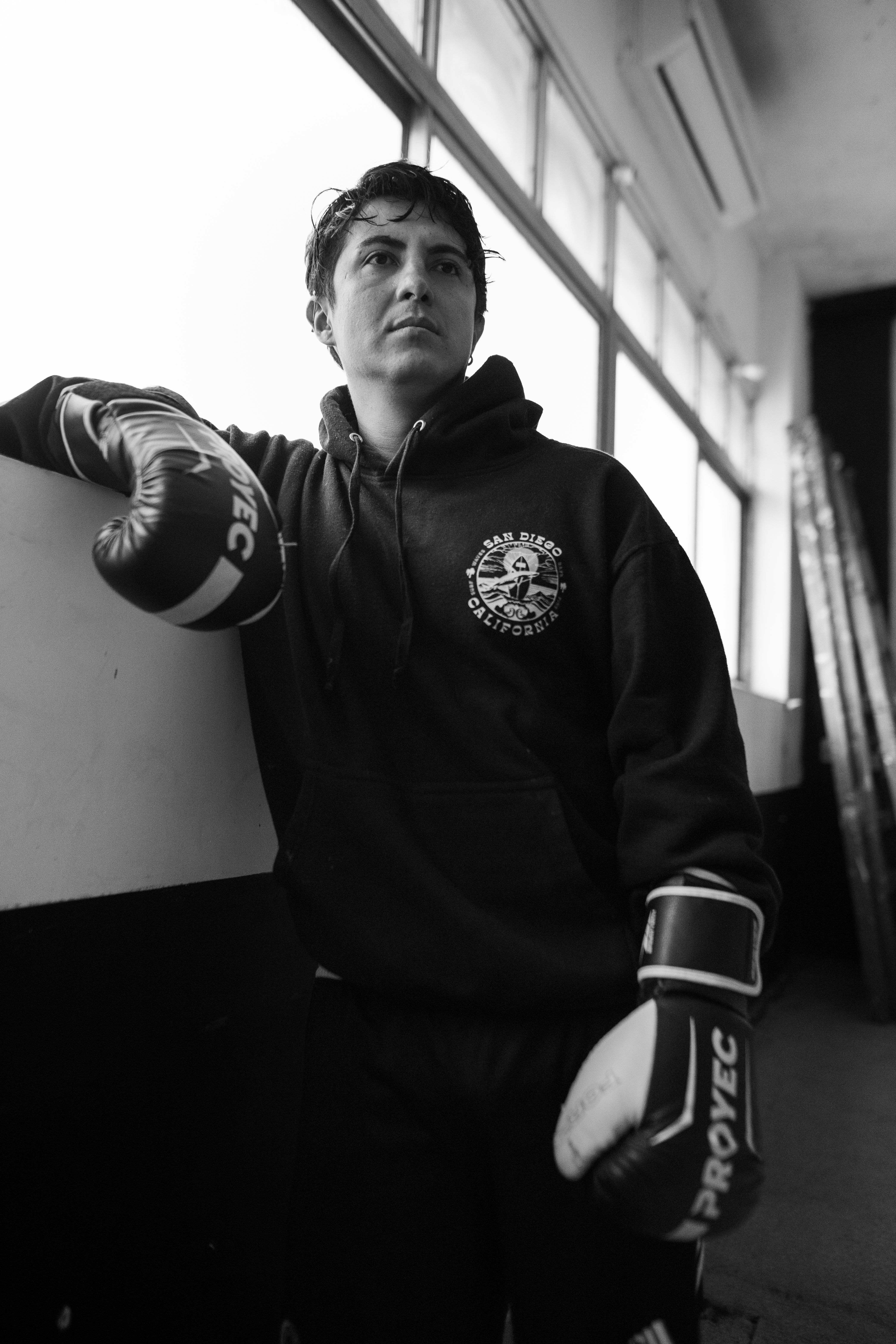 Focused boxer in a gym, captured in black and white, wearing gloves.