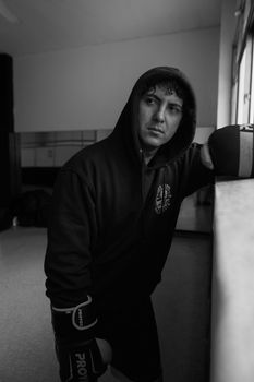 Black and white image of a boxer in a hoodie resting inside a gym.