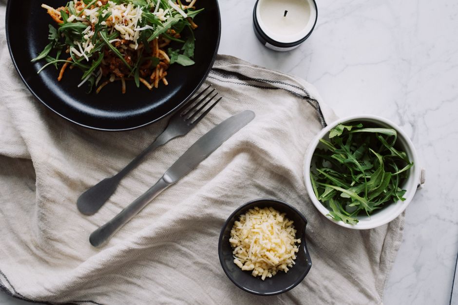 Top view of tasty vegetable salad served on black plate with fork and knife placed on white napkin near candle and cup with herb