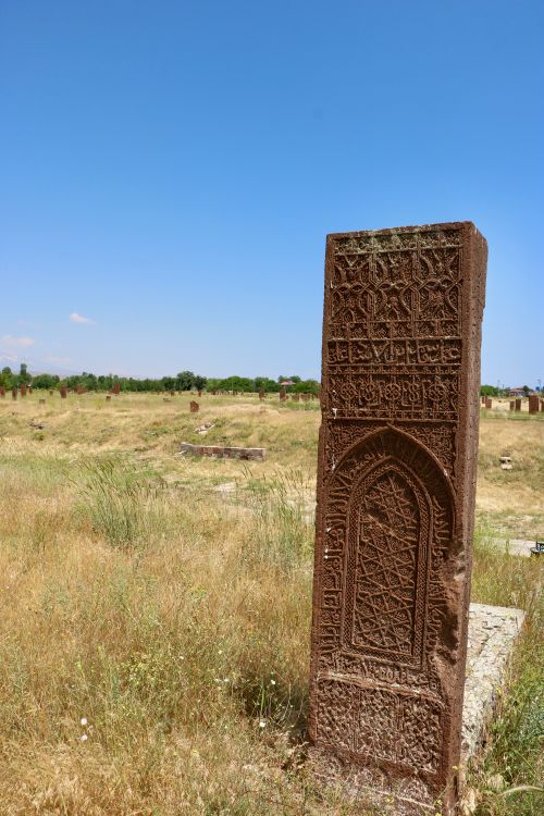 Free Ancient engraved tombstone stands amidst open grassy landscape under a clear blue sky. Stock Photo