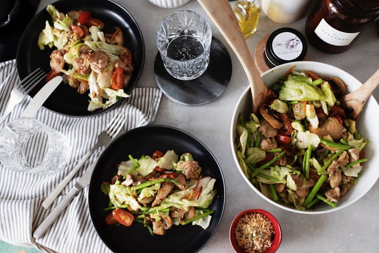 Fresh Salad Served On Black Plates From Big White Bowl On Table In Kitchen