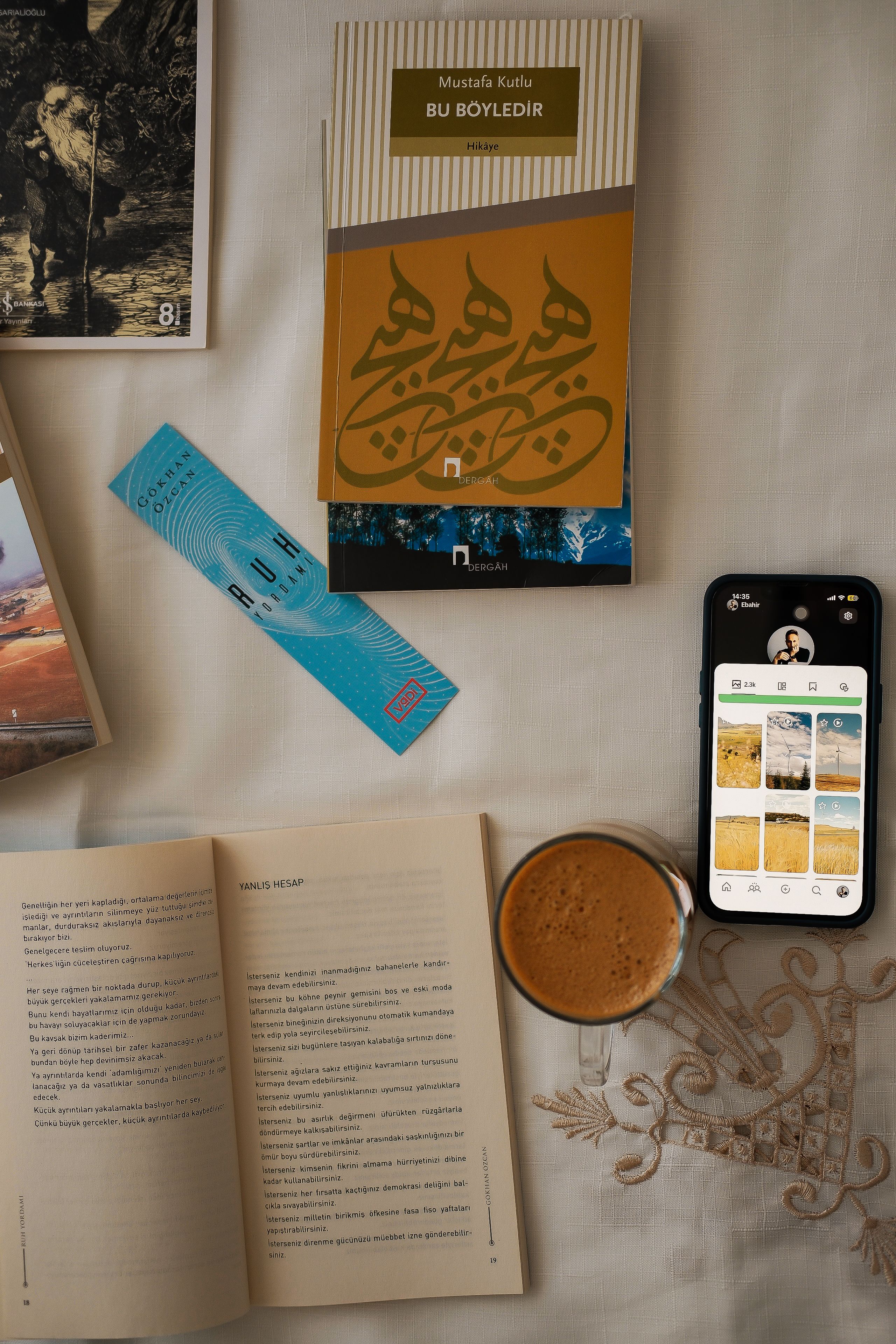 Flat lay of books, a smartphone, coffee, and a bookmark on a white tablecloth.