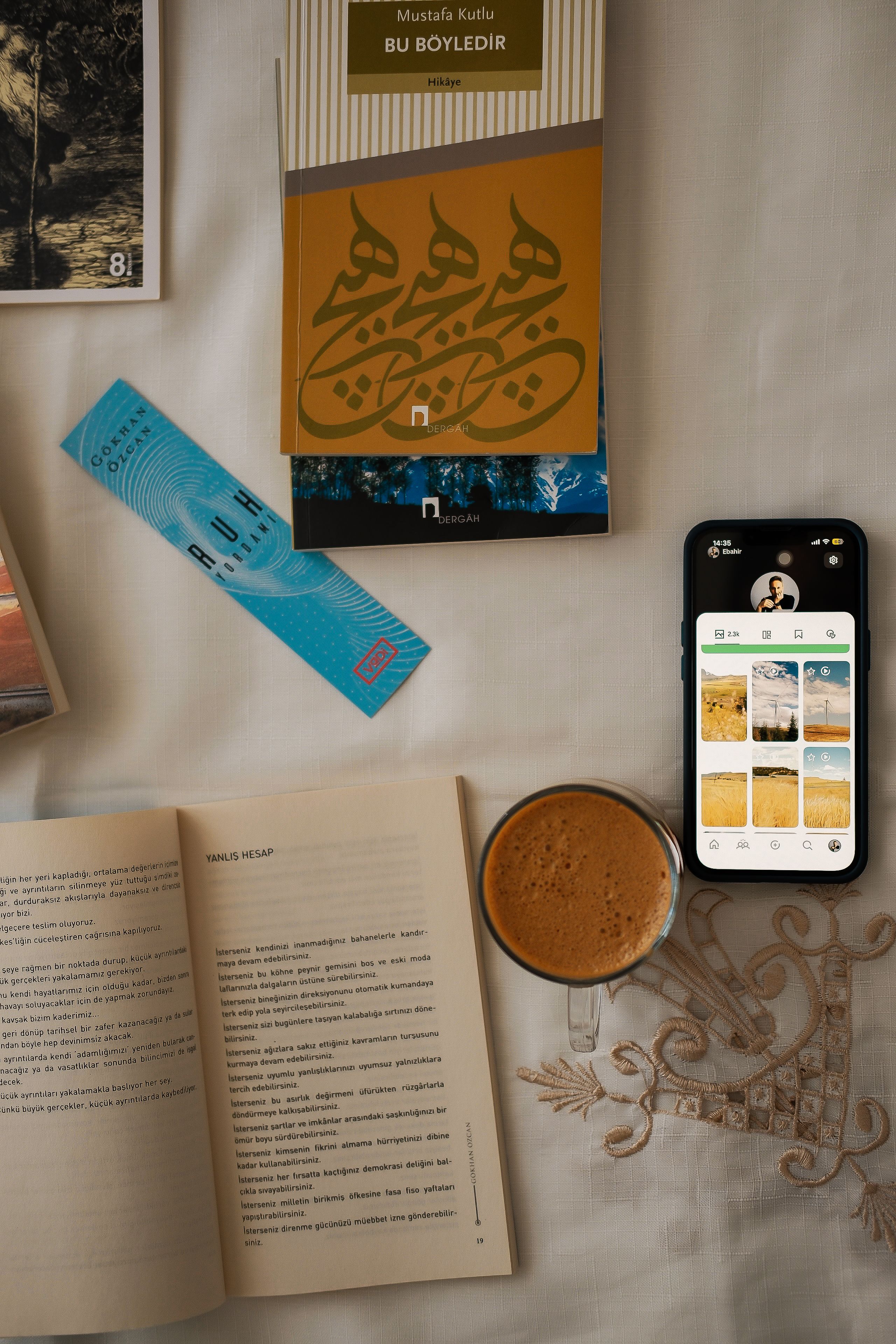 Overhead view of a cozy reading setup with open books, coffee, bookmark, and smartphone on a table.