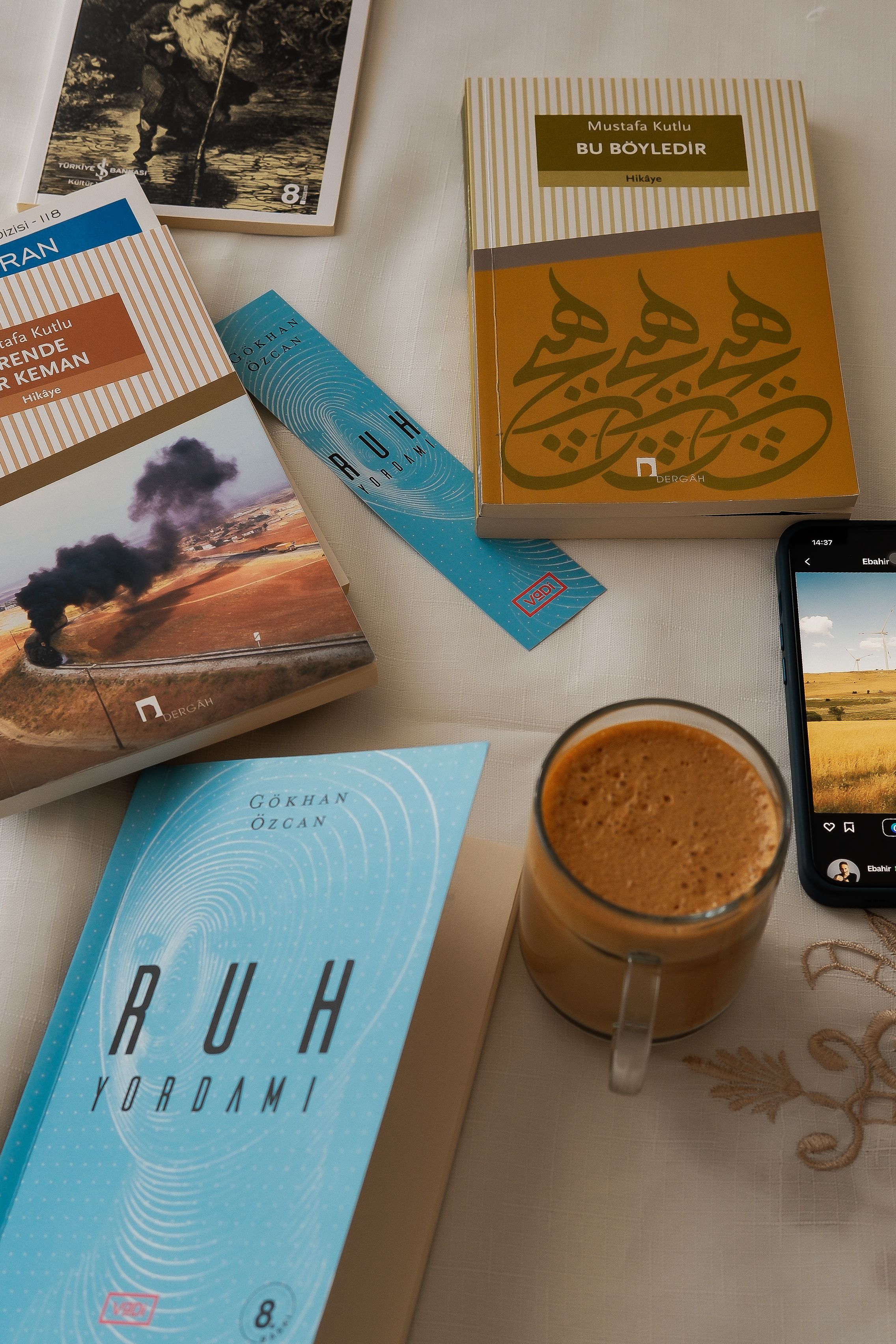 Warm afternoon setting with books, a glass of coffee, and a mobile phone on table.