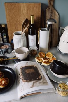 Delicious pancakes served on plates near opened book on table with various kitchenware and bootle of wine near cutting boards in light modern kitchen
