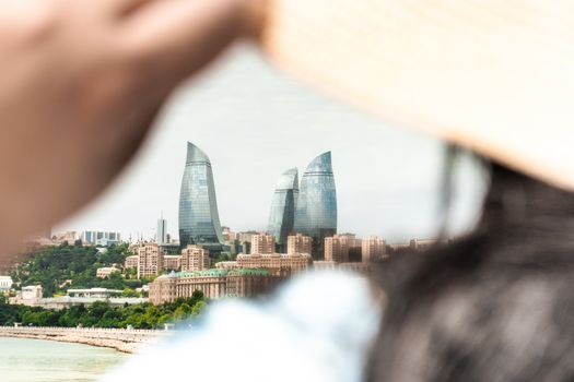 A scenic view of Baku's iconic Flame Towers seen through the perspective of a person adjusting a sunhat., free online jigsaw puzzle on JigsawPuzzlesFreeOnline.org