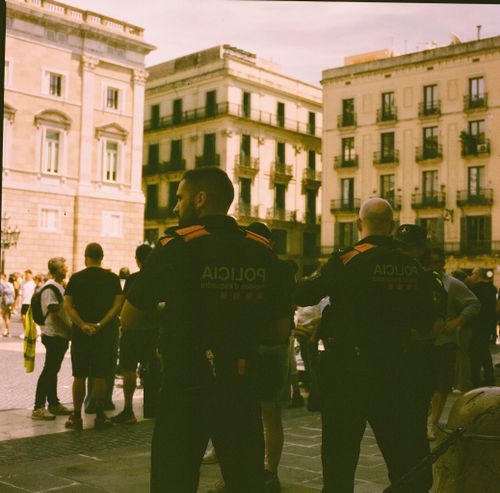 Free Police officers monitoring a crowded plaza in Barcelona, Spain, with historic buildings in the background. Stock Photo