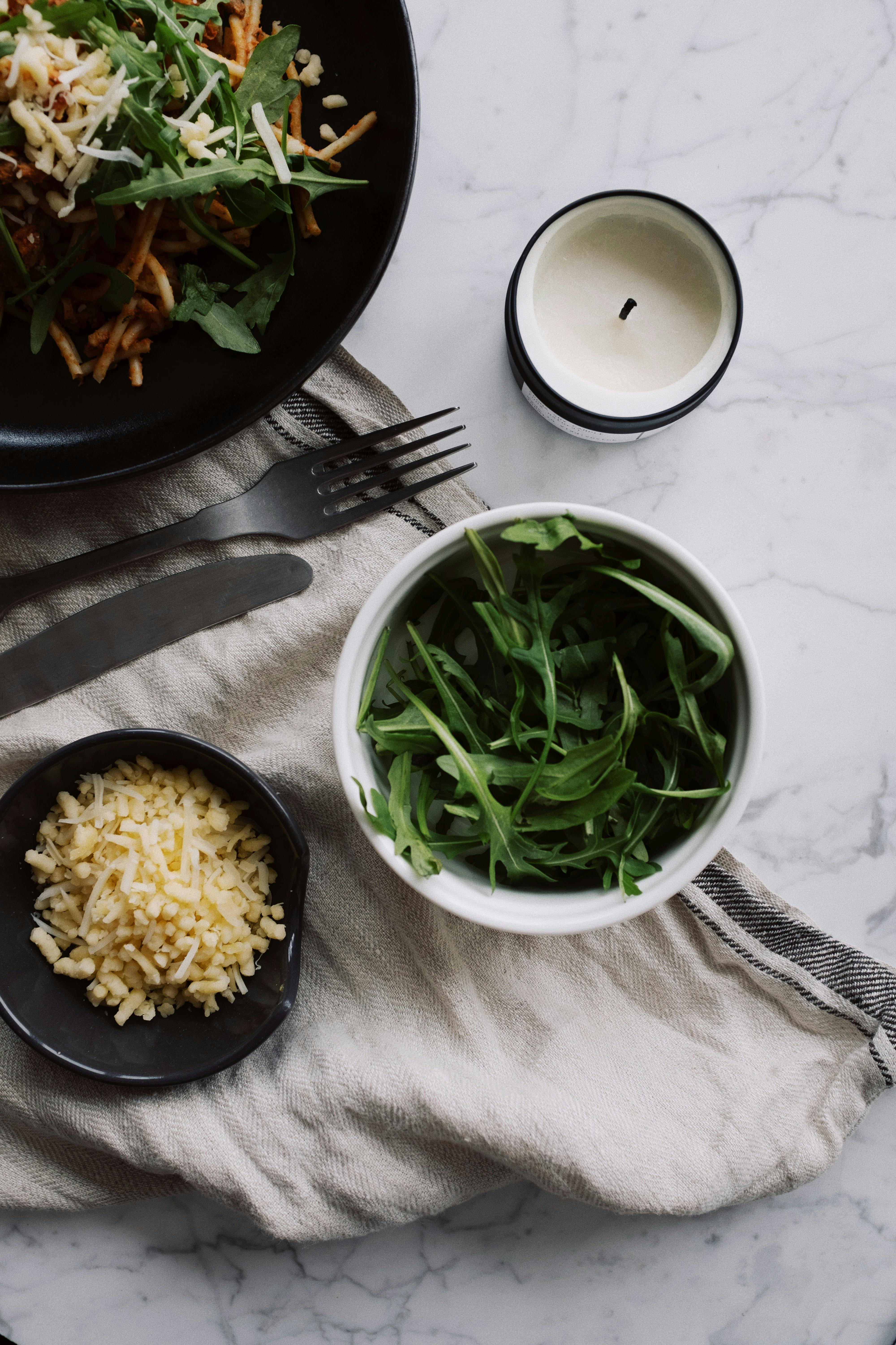 spaghetti bolognese next to bowls with cheese and arugula on table