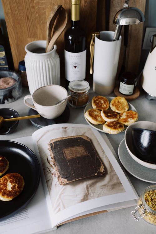 Free From above of plates with fresh cooked yummy cheese pancakes surrounded by kitchen utensils with opened magazine locating on countertop in kitchen during early morning Stock Photo