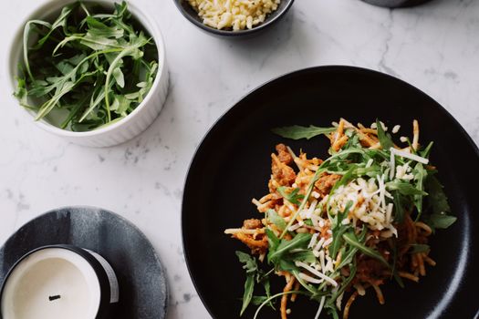 Plate of spaghetti topped with fresh arugula and shredded cheese on marble table.