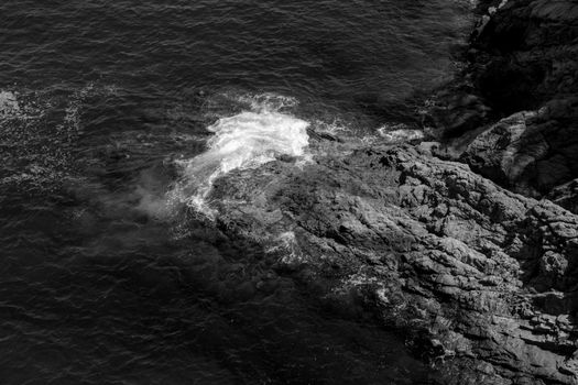 Waves crash on coastal rocks in Tossa de Mar, Spain, captured in black and white.