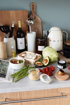 Assorted healthy food and vegetables placed on gray tabletop against kitchen utensils and appliances in cozy kitchen in apartment on sunny day