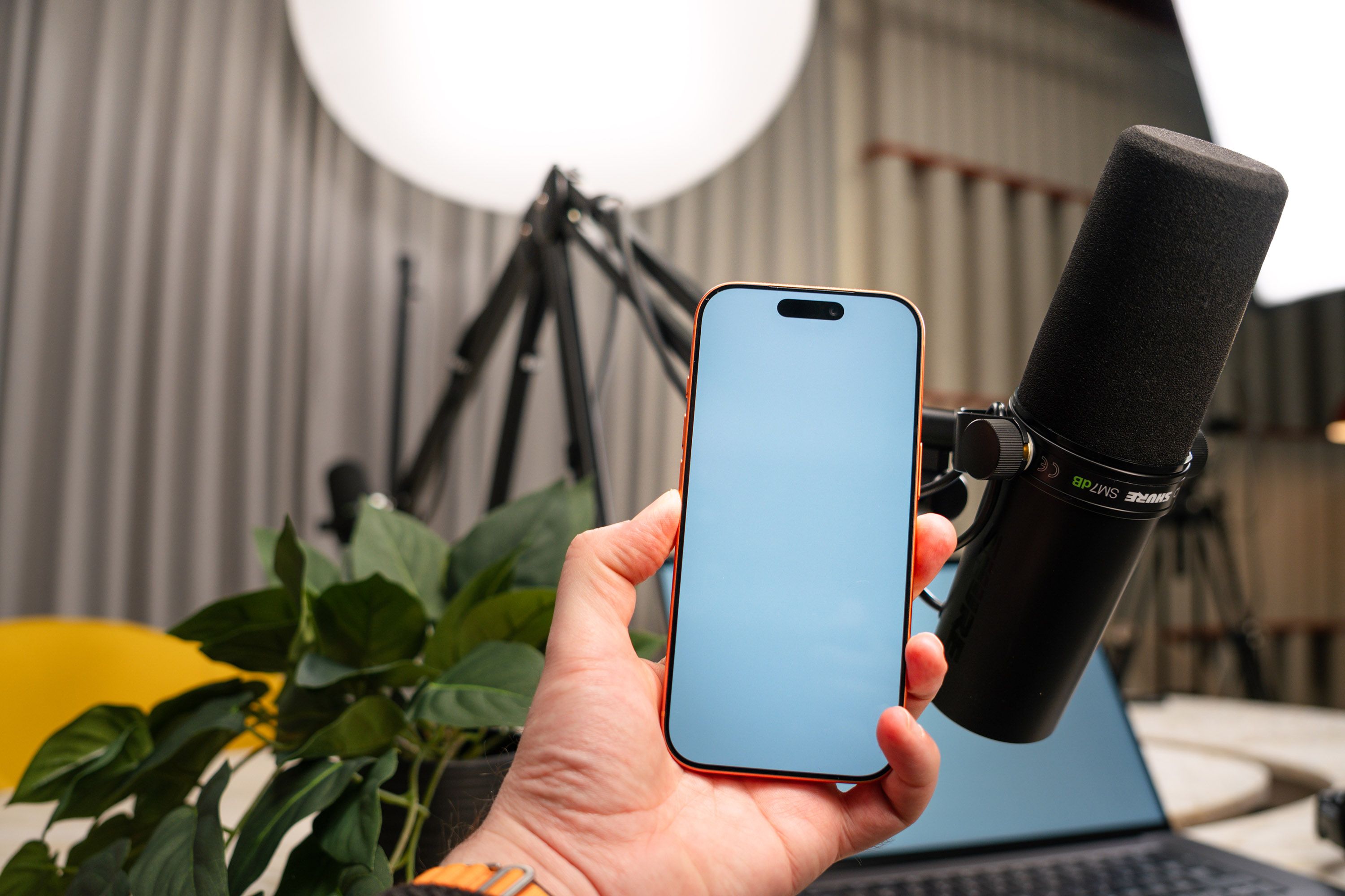 A podcast studio setup with a hand holding a smartphone and a professional microphone for recording.