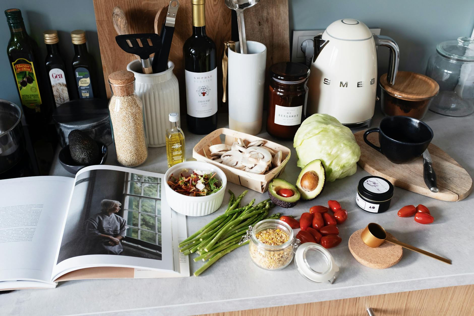 Various colorful healthy food and vegetables locating on countertop next to many different utensils and white kettle during cooking in stylish kitchen