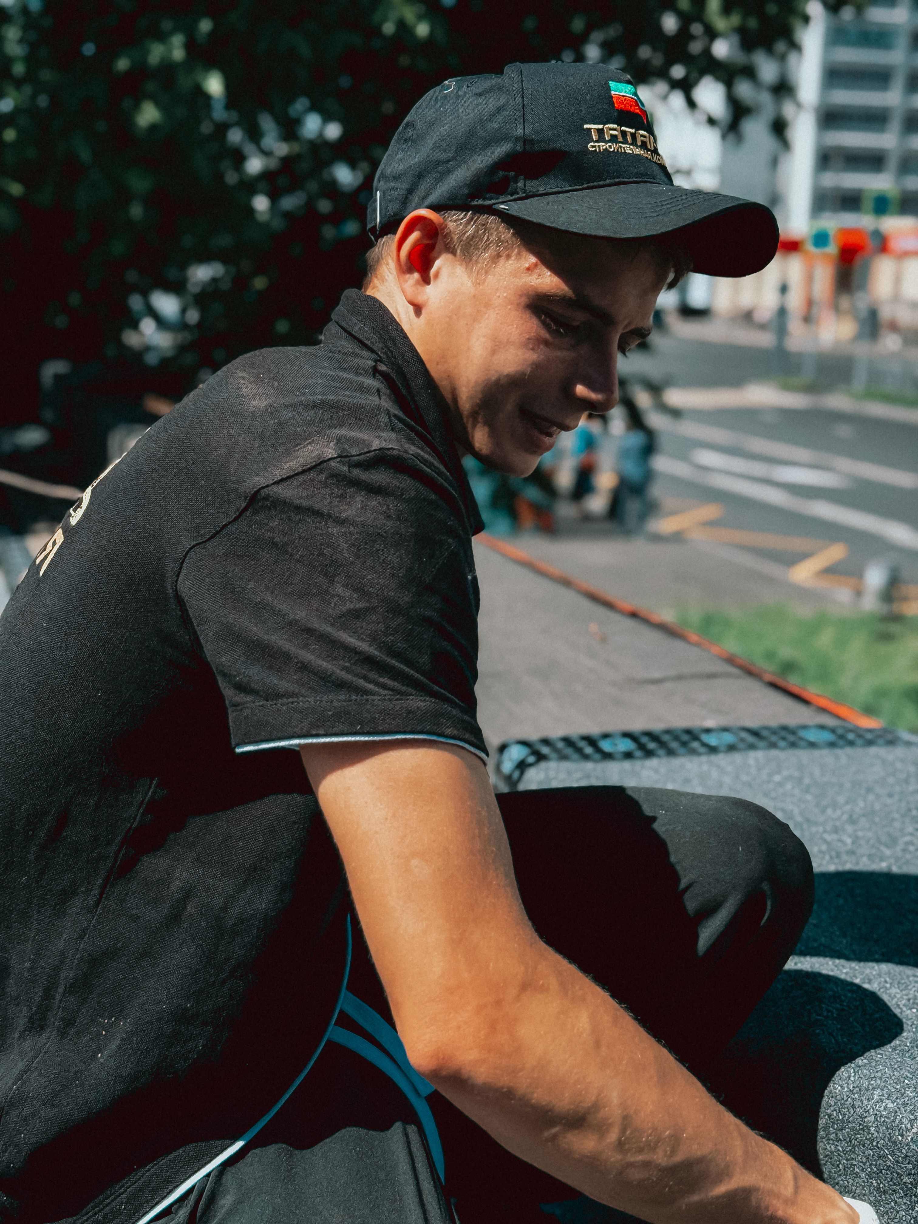 A young man wearing a black cap working on a city rooftop under sunlight.