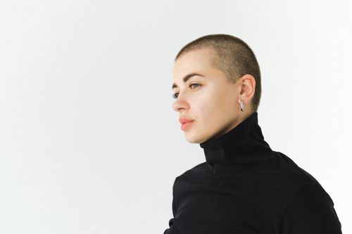 Free A thoughtful woman with a shaved head in a black turtleneck, looking pensive. Stock Photo
