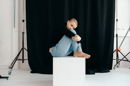 Free Woman In Black Long Sleeve Shirt and Blue Denim Jeans Sitting On A Cube Stock Photo