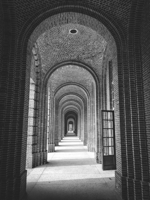 Free Stunning black and white photo of an elegant brick archway corridor with symmetrical design. Stock Photo