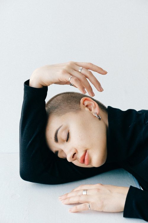 Free A peaceful portrait of a woman with a shaved head, eyes closed, leaning on a table in relaxation. Stock Photo