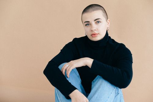 Free Minimalist portrait of a woman with short hair wearing a black sweater and jeans, captured in a studio setting. Stock Photo