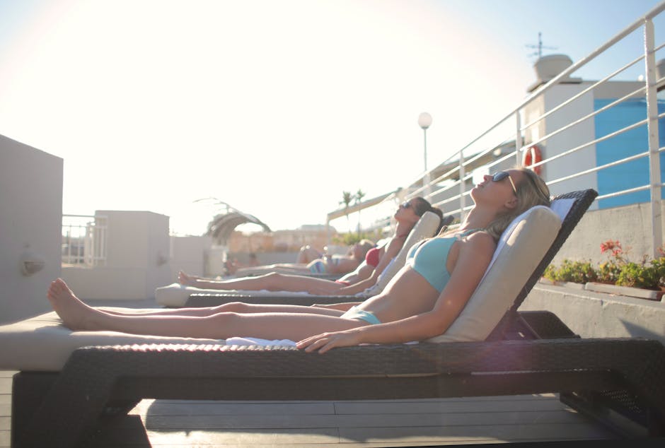 People sunbathing on rooftop loungers under the clear sky, enjoying a relaxing summer day.