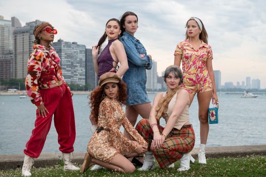 Group of diverse adults in retro outfits by a city waterfront, showcasing unique fashion styles.