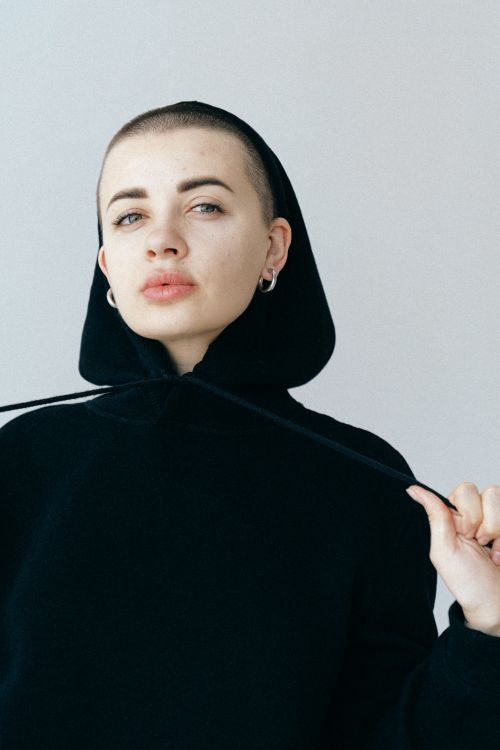 Free A close-up portrait of a confident woman wearing a black hoodie, showcasing modern fashion and bold expression. Stock Photo