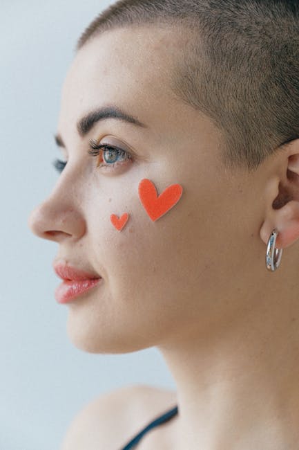 Portrait of attractive young female with short haircut and red stickers in form of hearts on face standing on gray background in studio and looking away