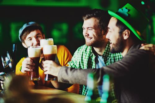 Free Three friends celebrate St. Patrick's Day with pints of beer at a lively pub. Stock Photo