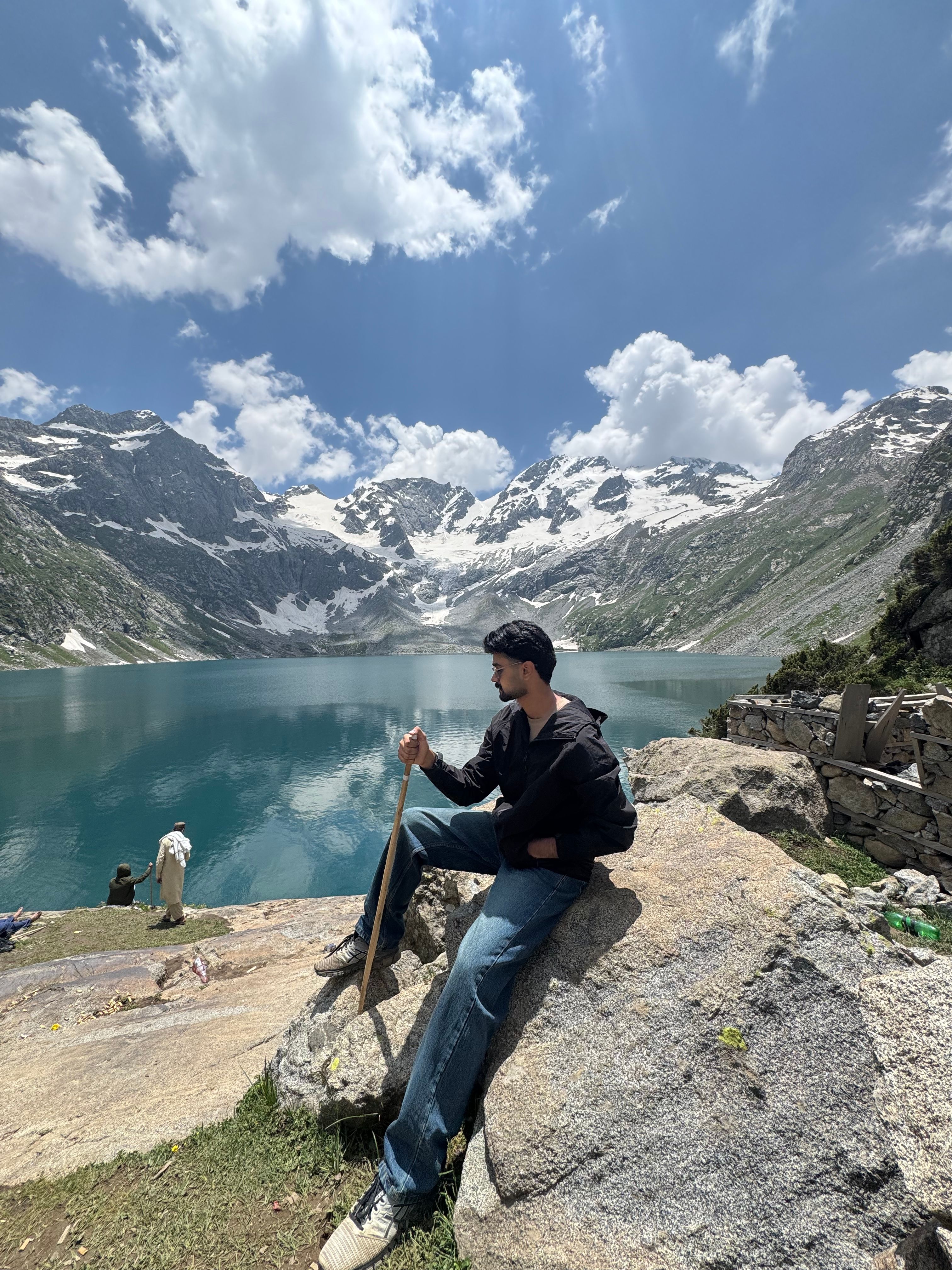 A man relaxing on a rock by a serene lake with snow-capped mountains in the background.
