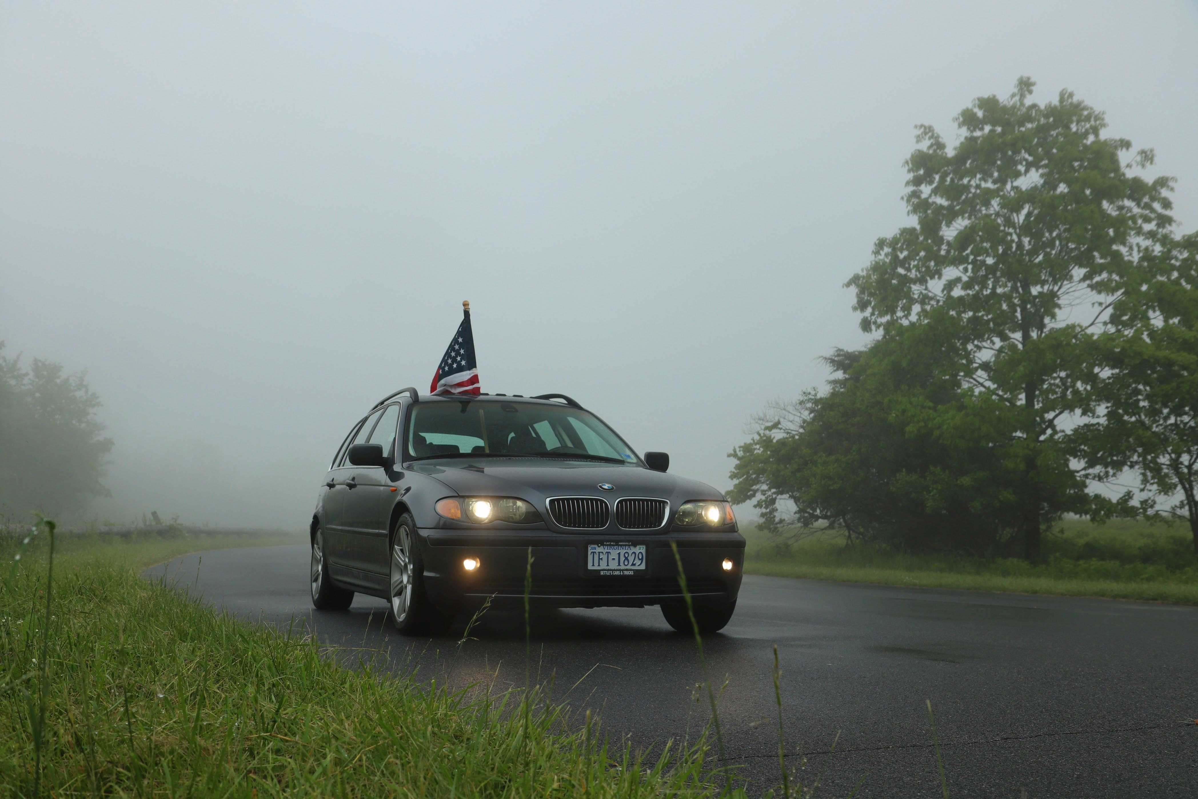 A car with an American flag on a foggy road surrounded by greenery.