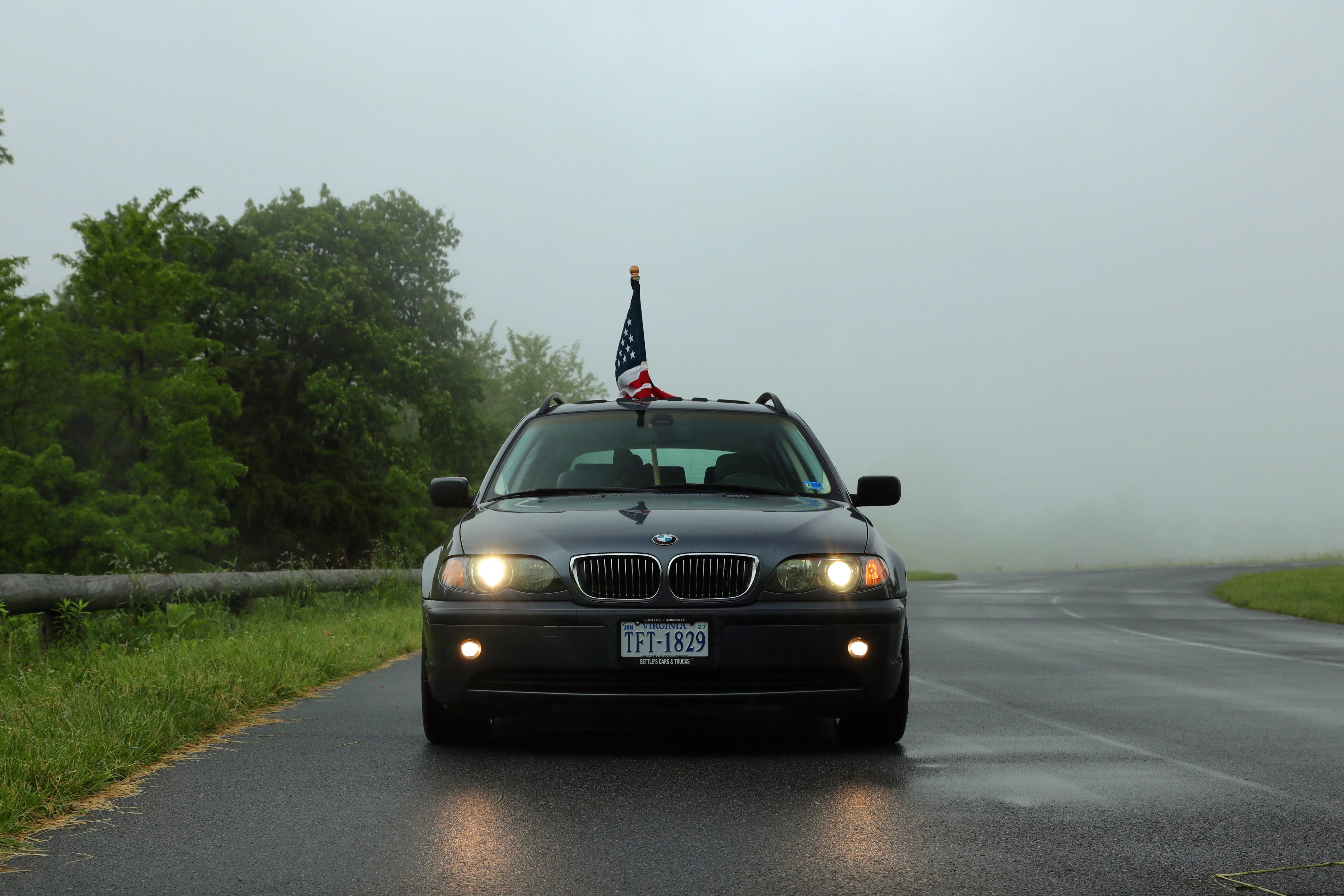 BMW car with American flag driving on a foggy, deserted road surrounded by greenery.