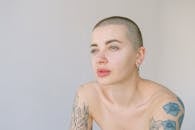 工作室特写肖像，一位留着平头、蓝眼睛的纹身女子看向别处