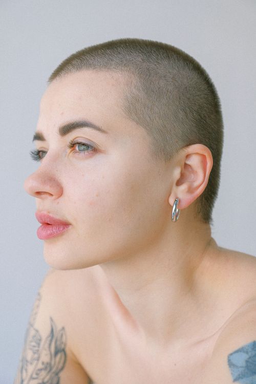 Free Side view of young short haired topless female with tattoos on arms looking away against gray background in light studio Stock Photo