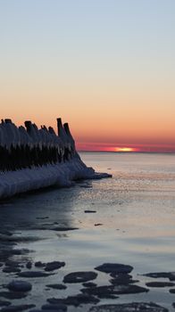 A stunning winter sunset over the icy shoreline, reflecting vibrant colors across the calm water.