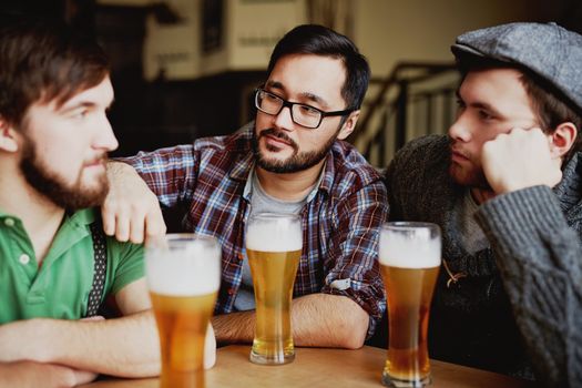 Three friends enjoy drinks and conversation at a cozy pub setting, showcasing camaraderie and leisure.