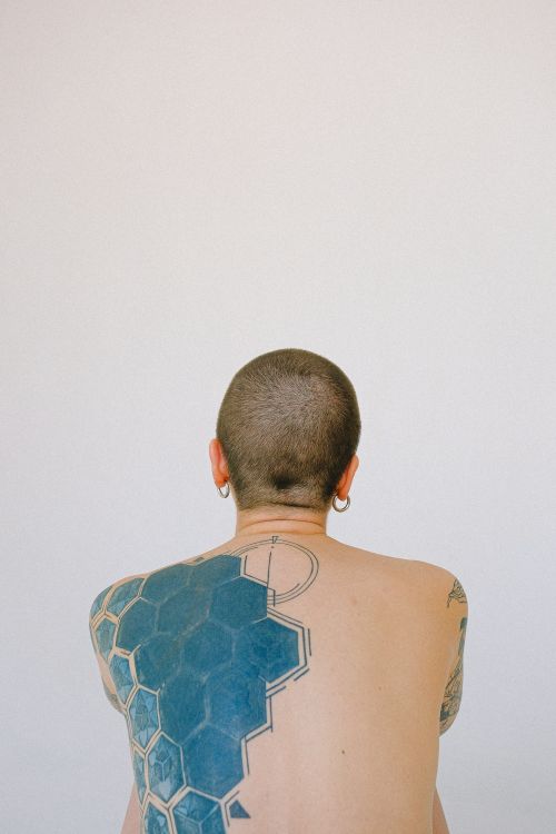 Free Shirtless person with geometric back tattoo and shaved head, facing away. Stock Photo