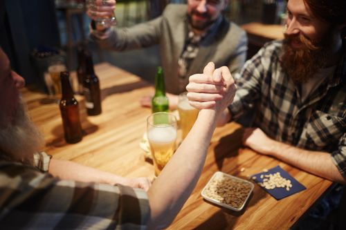 Free Friends enjoying a lively arm wrestling match and drinks at a pub. Stock Photo
